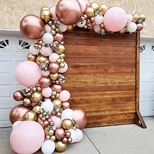 Balloon arch with pink, gold, and white balloons on wooden backdrop.