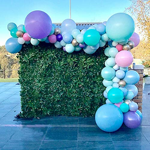 Colorful balloon garland on green leafy wall.