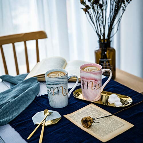 Two coffee mugs with latte art on a table with books and decor.