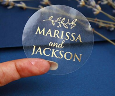 Hand holding a clear round sticker with gold lettering