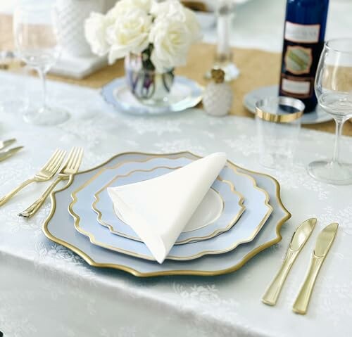 Elegant table setting with layered plates, gold cutlery, and white roses.