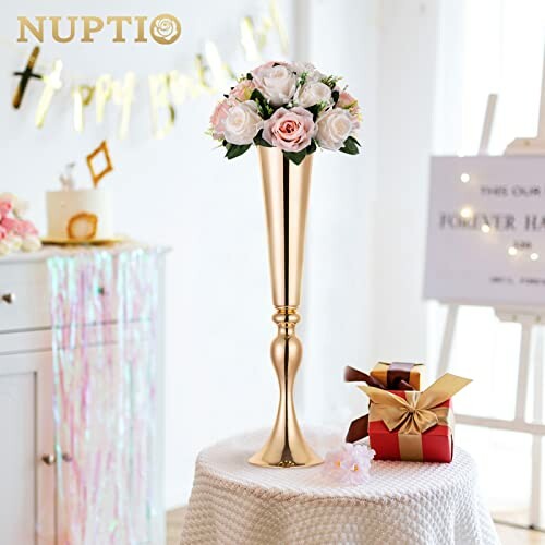 Tall gold vase with pink and white flowers on a decorated table.