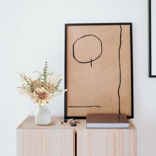 Minimalist art with a vase of flowers on a wooden cabinet.