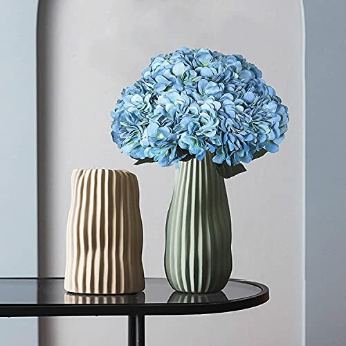 Two modern vases with blue flowers on a table.