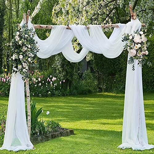 Wedding arch with white fabric and floral decorations on a lawn.